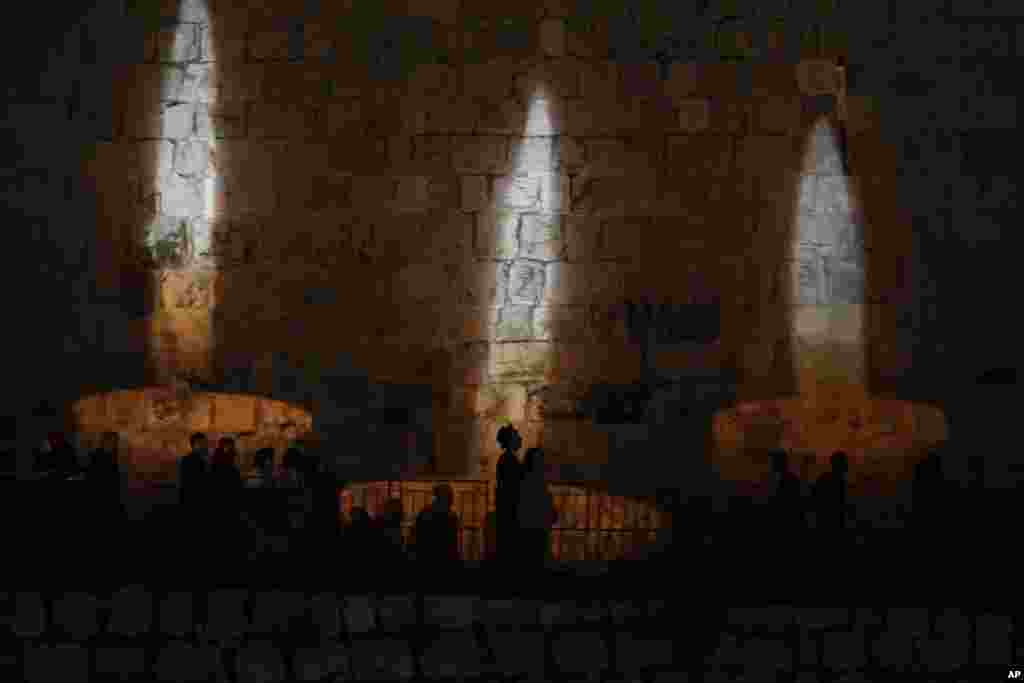 People walk by an image of memorial candles, projected on the walls of Jerusalem's Old City on the eve of annual Holocaust Remembrance Day, April 17, 2023. 