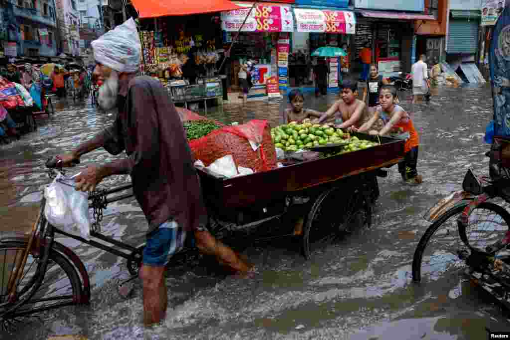 Children push a vegetable seller&#39;s cart as streets are flooded amid heavy rains in Dhaka, Bangladesh.