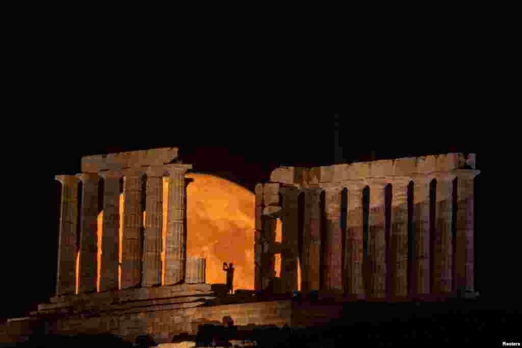 A person takes a photo as a full moon known as the "Buck Moon" rises behind the Temple of Poseidon, in Cape Sounion, near Athens, Greece, July 3, 2023. 
