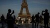 FILE - People use their smartphones near the Olympic rings displayed on the Eiffel Tower in Paris, June 7, 2024.