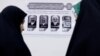 Iranian women stand near a paper showing the presidential candidates during the election to choose a successor to Ebrahim Raisi following his death in a helicopter crash, at the Iranian consulate in Najaf, Iraq, June 28, 2024. 