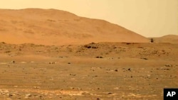 Slika koju je 30. aprila 2021., napravio rover Mars Perseverance prikazuje helikopter Ingenuity, desno, kako leti iznad površine. Podaci prikupljeni sa planete ukazuju da bi ispid površine moglo biti dosta vode. (NASA preko AP)