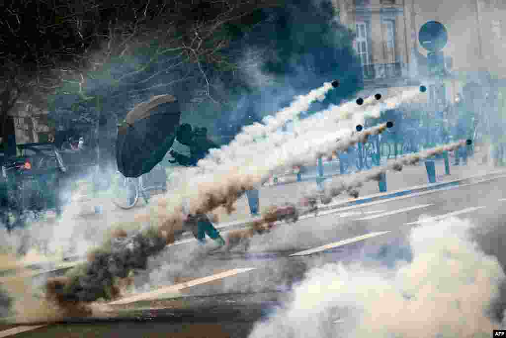 A protester holds an umbrella amid tear gas fired by security personnel during the 8th day of strikes and protests across the country over the government&#39;s proposed pension overhaul, in Nantes, France.