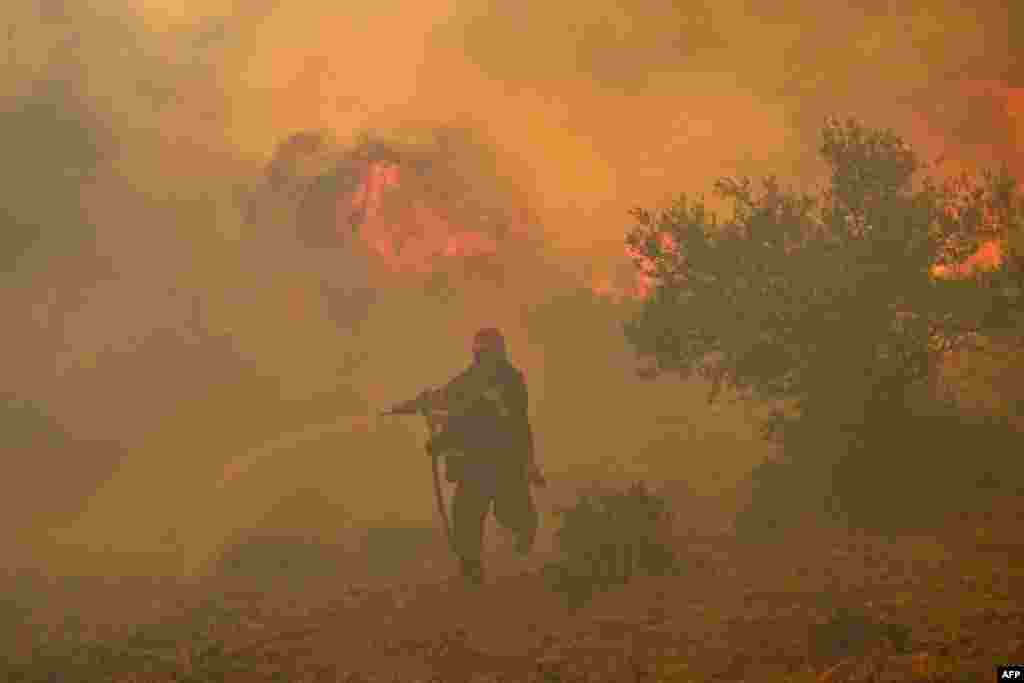 A fireman runs away from blazes as he tries to control a wildfire in New Peramos, near Athens, Greece. Firefighters battled blazes in parts of Greece and the Canary Islands, while Spain issued heat alerts, and some children in Italy's Sardinia were told to avoid playing sports.