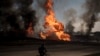 FILE - A man rides his bike past flames and smoke rising from a fire following a Russian attack in Kharkiv, Ukraine, March 25, 2022. 