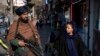 FILE - A Taliban fighter stands guard as a woman walks past in Kabul, Afghanistan, Dec. 26, 2022. 