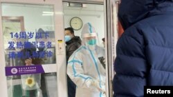 2022年12月15日，一名男子在北京一家医院的发热门诊门外排队等待。一位身着防护服的医务人员正准备关门。中国有关当局毫无预兆地宣布解封后，新冠肺炎的感染人数和死亡人数不断增加，引起人们的恐慌。