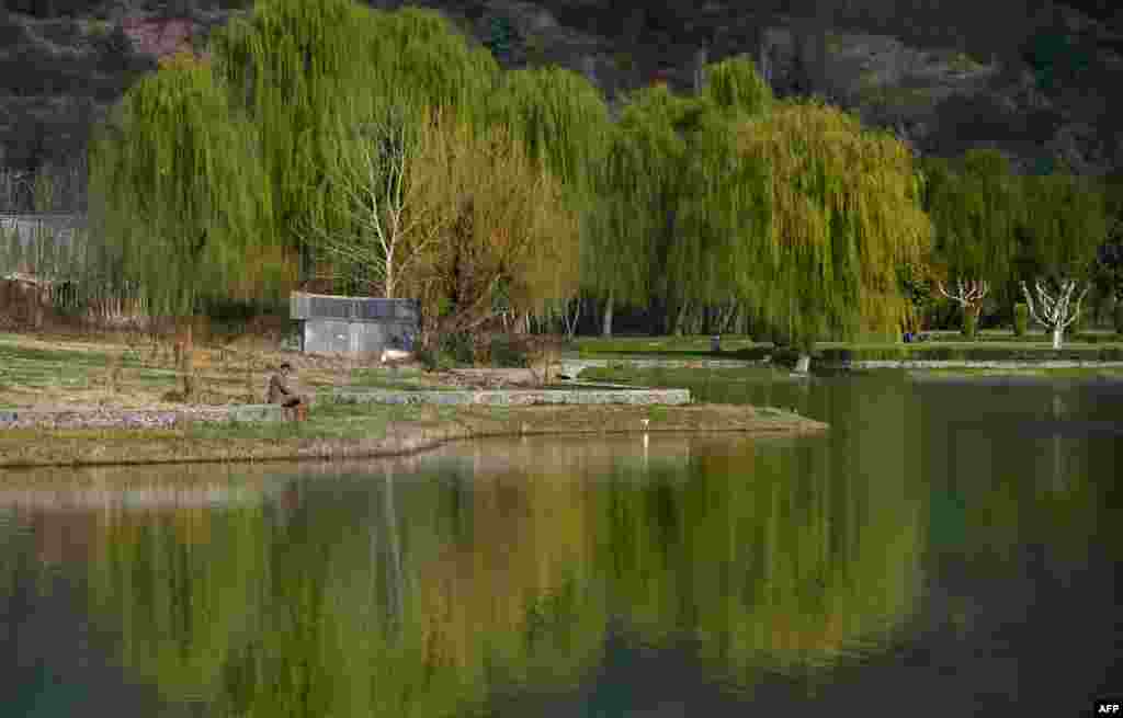 An Indian Kashmiri man sits by a lake in a garden by the Zabarwan Hills in Srinagar.