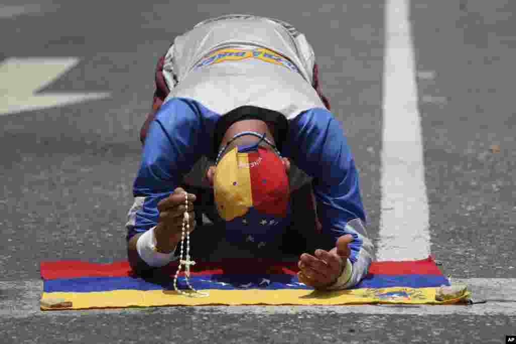 Seorang demonstran yang membawa rosario berdoa di atas bendera nasional Venezuela, sebelum aksi protes menentang Presiden Nicolas Maduro di Caracas.
