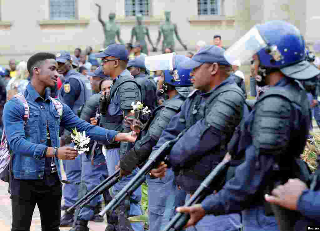 Seorang mahasiswa menawarkan bunga kepada para polisi dalam bentrokan saat demonstrasi di kampus Universitas Witwatersrand, Johannesburg, Afrika Selatan.