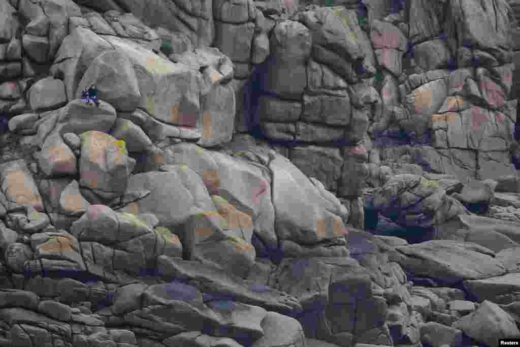 People sit on large rocks on the Britanny coast in Perros-Guirec, France.