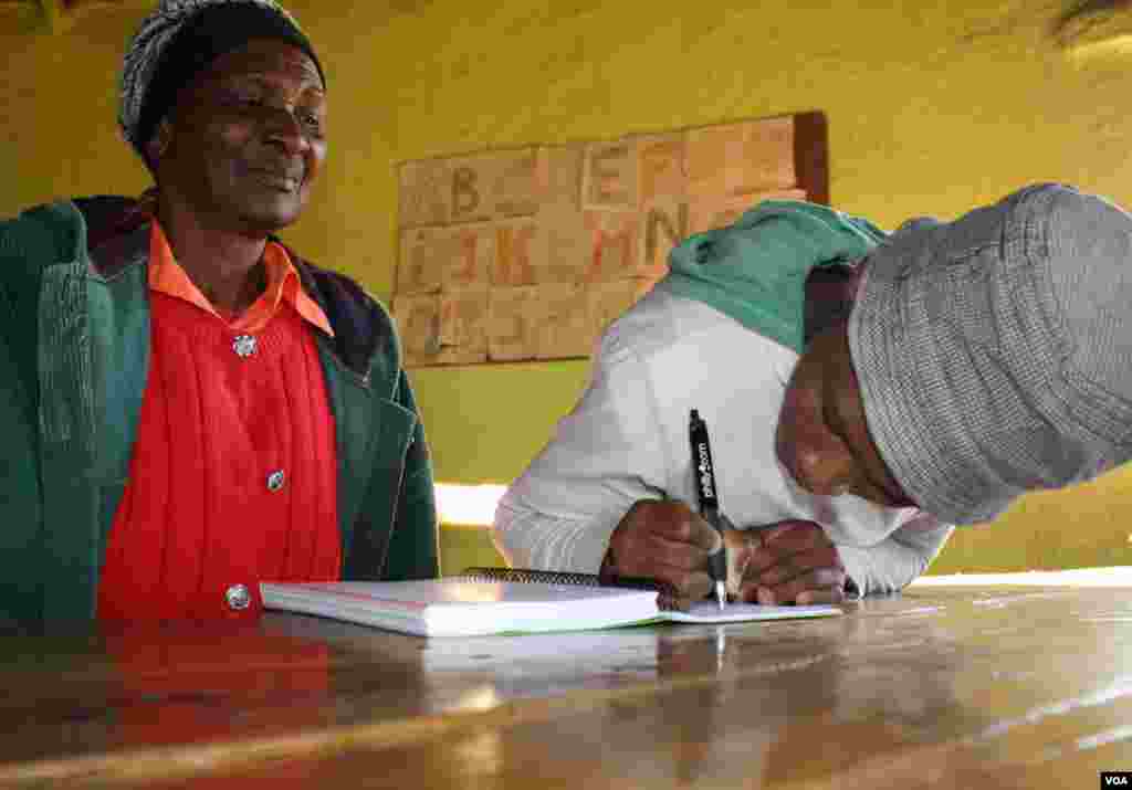 Sinesipho Makala writes her name, watched by her grandmother, Nozinzile (VOA/ D. Taylor)