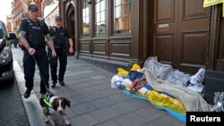 FILE - Police officers walk past a homeless man in Windsor, Britain, Oct. 10, 2018. About 50 homeless people have secured employment training through a crowdfunding campaign by social enterprise Beam. 