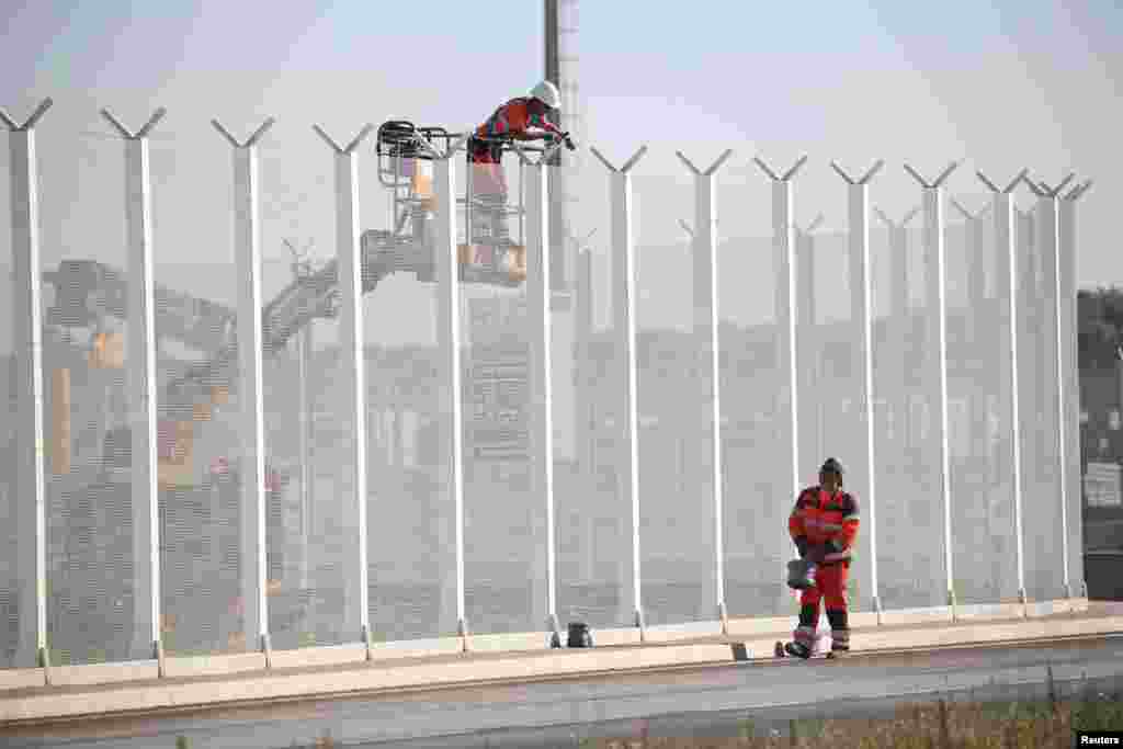 Para pekerja memasang kabel listrik pada pagar sepanjang pelabuhan di kota Calais, Perancis untuk mencegah migran melompat ke atas truk.