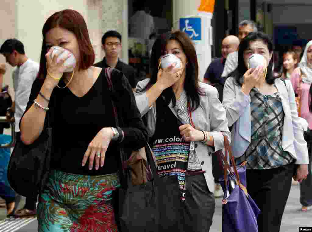 Para wanita menutupi wajah-wajah mereka dengan masker ketika kabut menyelimuti distrik pusat bisnis Singapura.