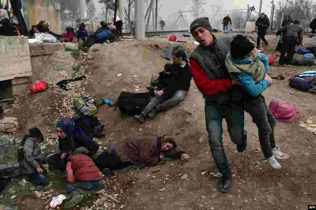A man evacuates a boy, while other migrants and refugees lay on the ground after Macedonian police fired tear gas at hundreds of Iraqi and Syrian migrants who tried to break through the Greek border fence in Idomeni.