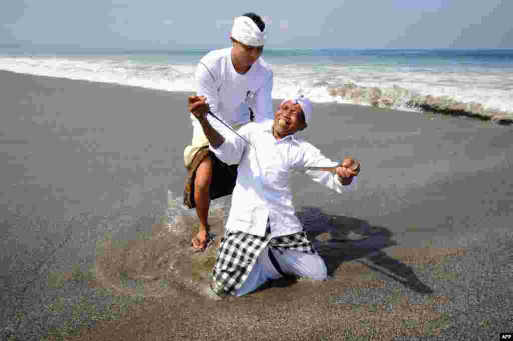 Seorang laki-laki Bali dalam keadaan trans menusuk dirinya dengan keris saat mengikuti upacara keagamaan Melasti di Pantai Petitenget di Kuta, Bali. Melasti adalah upacara penyucian yang diadakan beberapa hari sebelum Nyepi, hari Tahun Baru umat Hindu yang diperingati dengan keheningan, di mana umat Hindu di Pulau Bali tidak diperbolehkan untuk bekerja, bepergian atau bersenang-bersenang. &nbsp;
