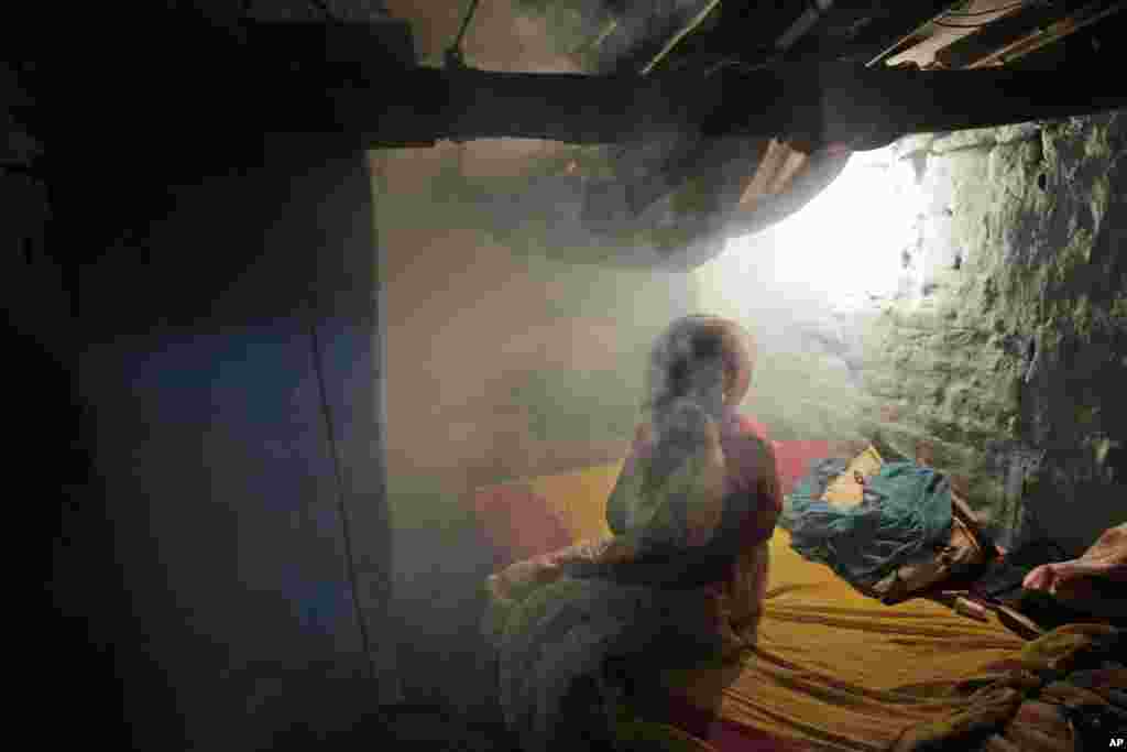 Seorang wanita duduk di dalam rumah yang diliputi asap dari proses fumigasi di Allahabad, India.&nbsp; Meskipun atas usaha yang dilakukan, termasuk menyemprot daerah yang cukup luas dengan campuran bahan bakar solar dan insektisida, di beberapa kota India untuk menanggulangi demam berdarah dan penyakit lainnya yang ditularkan oleh nyamuk setiap tahunnya selama musim hujan.