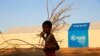 FILE - A refugee walks past a World Food Program tent at Um-Rakoba camp, in al-Qadarif state, Sudan, Nov. 23, 2020.