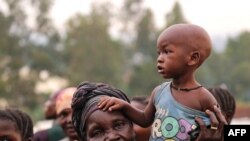 FILE - A woman holds a child on her shoulders in an internally displaced persons camp outside the town of Bunia, in Ituri province, June 21, 2019.