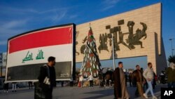 Iračani šetaju oko božićne jelke ukrašene predmetima koji liče na djecu umotanu u pokrove u znak solidarnosti s Palestincima u Gazi, na trgu Tahrir u Bagdadu, Irak, u nedjelju, 31. decembra 2023. (AP Photo/Hadi Mizban)