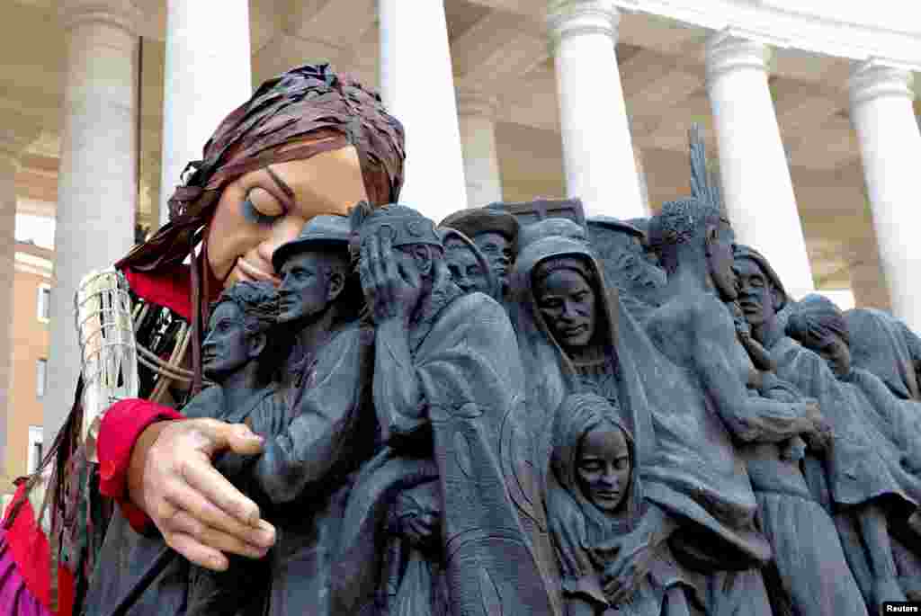 Little Amal, a 3.5-meter-tall puppet of a young Syrian refugee girl, embraces the Angels Unawares scuplure in St. Peter's Square at the Vatican, as she travels across Europe to raise awareness for the plight of young refugees.