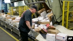 FILE - Steve Robino arranges packages on a conveyor belt at the main post office in Omaha, Neb., Dec. 14, 2017.