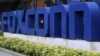 FILE - A worker looks out through the logo at the entrance of the Foxconn complex in the southern Chinese city of Shenzhen, May 27, 2010. 