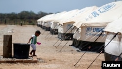 FILE - A Venezuelan migrant child walks next to a water tank, in a camp run by the U.N. refugee agency UNHCR, in Maicao, Colombia, May 6, 2019.