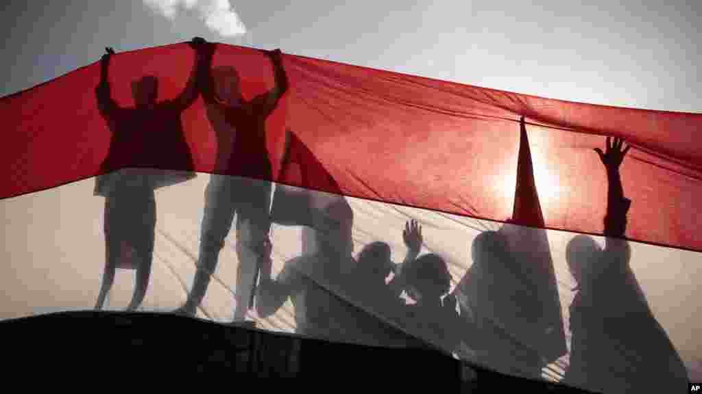 Siluet para pemuda memegang bendera Yaman ukuran raksasa pada peringatan Revolusi Yaman Utara ke-54 di Sana&#39;a.