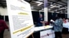 A list of benefits flanks Jon Stembridge, center, a human resource and safety manager with HomeStretch, a domestic manufacturer of upholstered reclining furniture, as he welcomes a potential applicant to his company's recruiting booth, Miss., Oct. 12, 2021. 