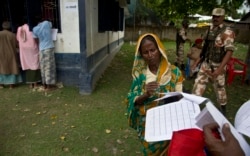 FILE - A woman checks her papers as villagers check their names in the final list of National Register of Citizens in Morigaon district, Assam, India, Aug. 31, 2019.