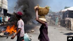 Machann kap pase tou pre yon barikad anflame pandan manifestasyon opozisyon politik la nan Pòtoprens. 9 jiyè 2018. (Foto: AP/Dieu Nalio Chery)