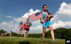 FILE - Girl Scouts Sarah and Megan Lontoc, 10, carry flags as the scouts placed thousands of flags on veteran's graves at Brig. Gen. William C. Doyle Veterans Memorial Cemetery in honor of Memorial Day in Wrightstown, N.J., May 27, 2016.
