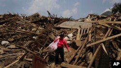 A woman carries her salvaged goods through the rubble of destroyed houses following a massive earthquake in the town of Longtoushan in Ludian County in southwest China's Yunnan Province Wednesday, Aug. 6, 2014.