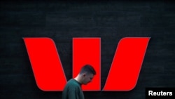 FILE - A pedestrian looks at his phone as he walks past a logo for Australia's Westpac Banking Corp outside a branch in central Sydney, Nov. 5, 2018.