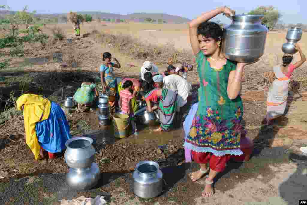 Indian Lambadi tribal villagers fill containers with drinking water from a leaking pipe on a roadside at Chandampet Mandal in Nalgonda east of Hyderabad in the southern Indian state of Telangana.