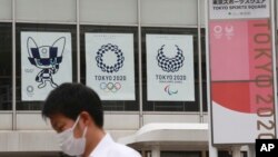 A man wearing a face mask to protect against the spread of the coronavirus walks by posters to promote the Tokyo Olympic Games in Tokyo Monday, June 7, 2021. (AP Photo/Koji Sasahara)