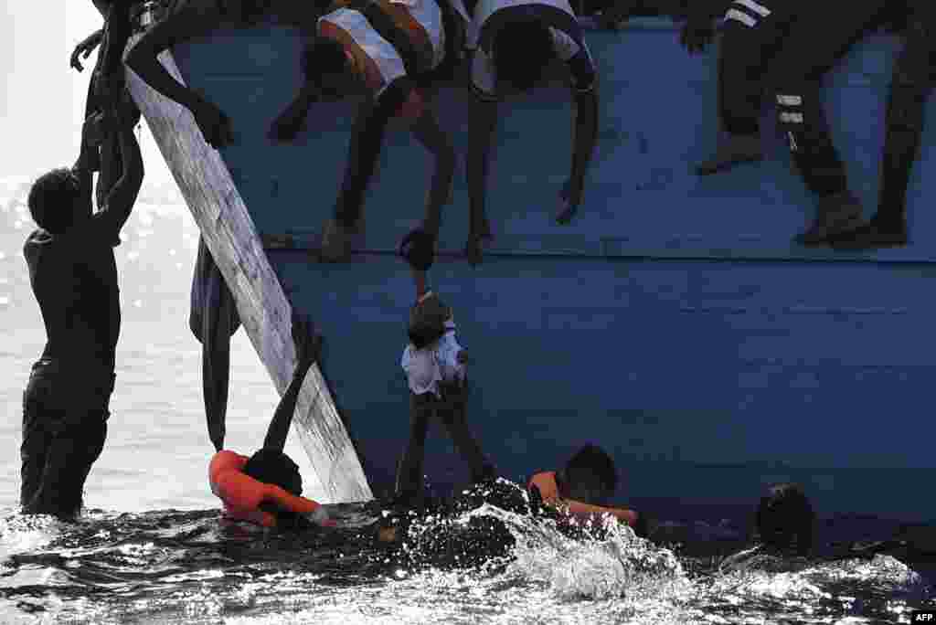 Migrants try to pull a child out of the water as they wait to be rescued by members of Proactiva Open Arms NGO in the Mediterranean Sea, some 12 nautical miles north of Libya, Oct. 4, 2016.