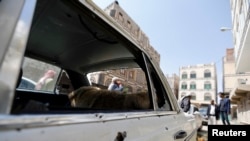 People gather near a car damaged by a mortar shell during fighting between Shi'ite Houthi militants and government forces in Sanaa September 19, 2014. 