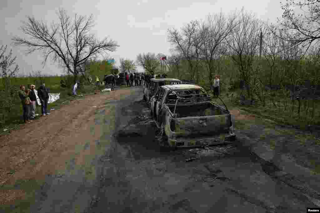 Warga lokal melihat mobil-mobil yang terbakar dekat pos pemeriksaan yang menjadi lokasi adu tembak dekat kota Slaviansk, Ukraina (20/4). (Reuters/Gleb Garanich)