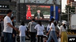 北京街头的行人观看电子屏幕上中国国家主席习近平通过视频在世卫大会视频开幕式上致辞。（2020年5月18日）