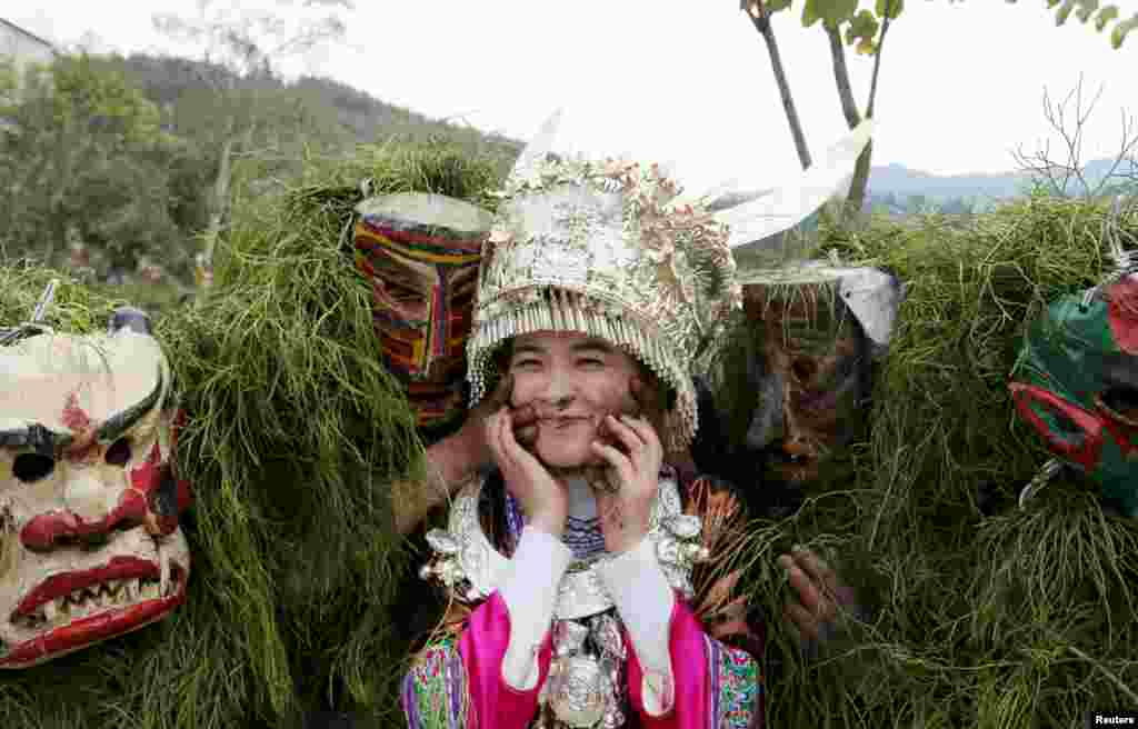 Ethnic Miao men wearing traditional masks smear dust on a woman&#39;s face to wish her good luck during a local celebration event for Lunar New Year in Liuzhou, Guangxi Zhuang Autonomous Region, China.