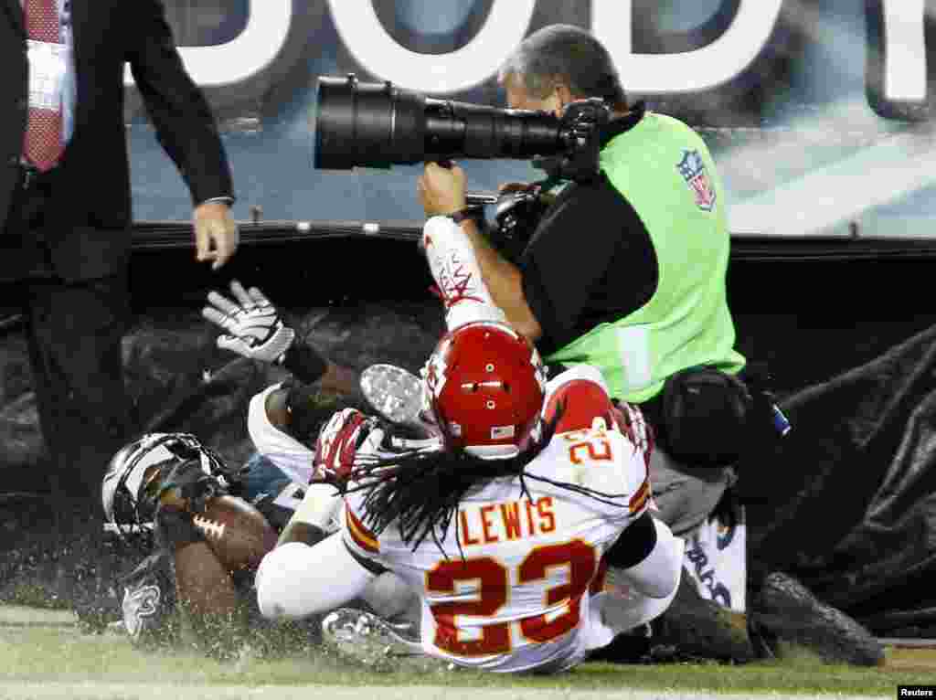 Pemain tim Eagle Filadelfia LeSean McCoy (25) dan anggota tim Chief Kansas City Kendrick Lewis (23) meluncur jatuh menimpa seorang fotografer di pinggir lapangan setelah McCoy mencetak gol selama kuartal keempat pertandingan sepak bola NFL di Philadelphia, Pennsylvania, 19 September 2013.