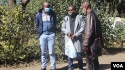 Journalists Samuel Takawira and Frank Chikowore stand with a police detective outside a court in Harare, Zimbabwe, May 23, 2020. (Columbus Mavhunga/VOA) 