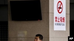 FILE - A Chinese man smokes in front of a pillar with a no smoking notice on display at a bus station in Beijing, March 24, 2011