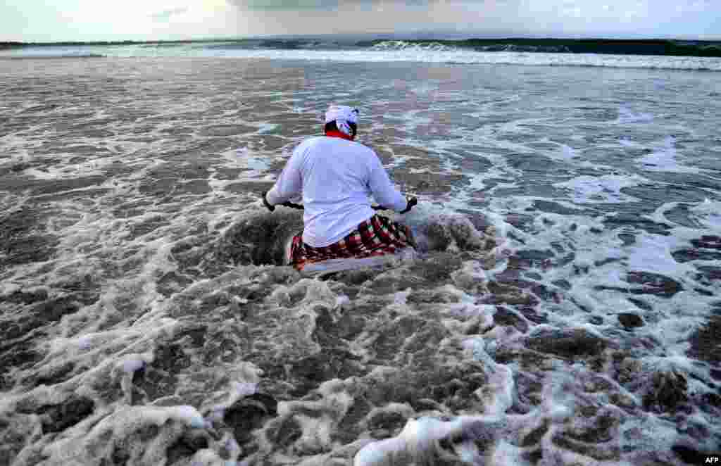 A Balinese man enters the water during a Melasti ceremony prayer at Petitenget beach near Denpasar on Bali island, Indonesia.