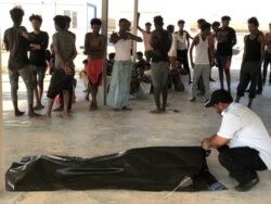 Migrants watch the body of their fellow migrant who died after a wooden boat capsized off the coast of Komas, a town east of the capital Tripoli, Libya, July 25, 2019.