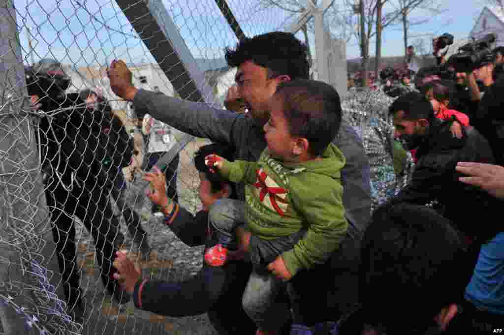 A man from Afghanistan carrying a baby cries as he pushes against the fence at the Greece-Macedonia border during a demonstration near the village of Idomeni, northern Greece, against Macedonia&#39;s refusal to allow Afghans to pass the border. Greece said that it was taking action to persuade Macedonia to take in Afghan migrants as thousands remained stranded at the border and the main port in Athens.