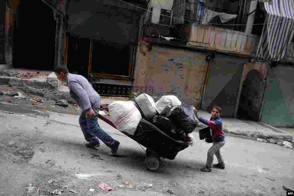 Dua remaja Suriah mendorong kereta yang berisi barang-barang mereka meninggalkan distrik Sheikh Maqsud di kota Aleppo. 